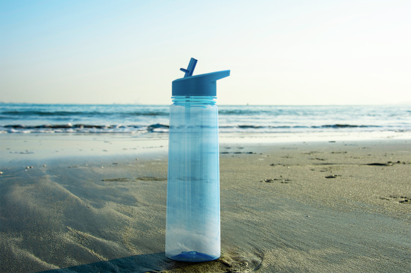 The after image of a blue water bottle on a sandy beach.