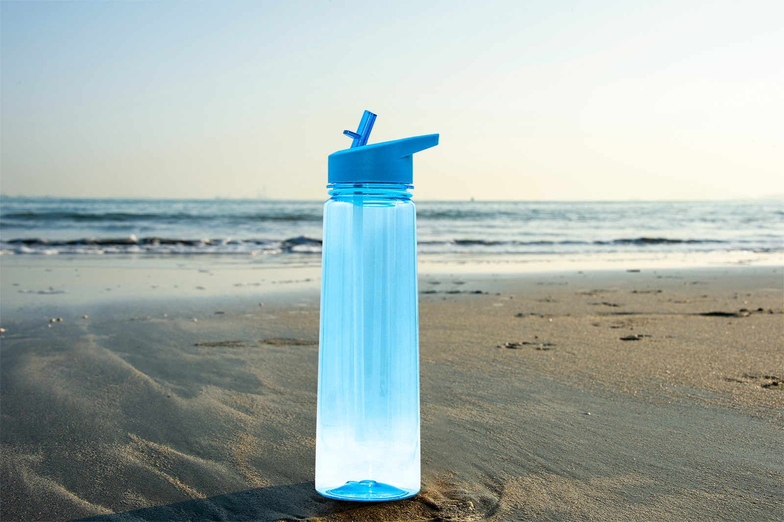 The before image of a blue water bottle on a sandy beach.